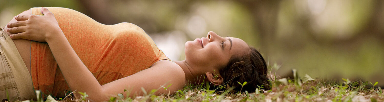 A pregnant woman lies on grass, her hand resting on her belly.