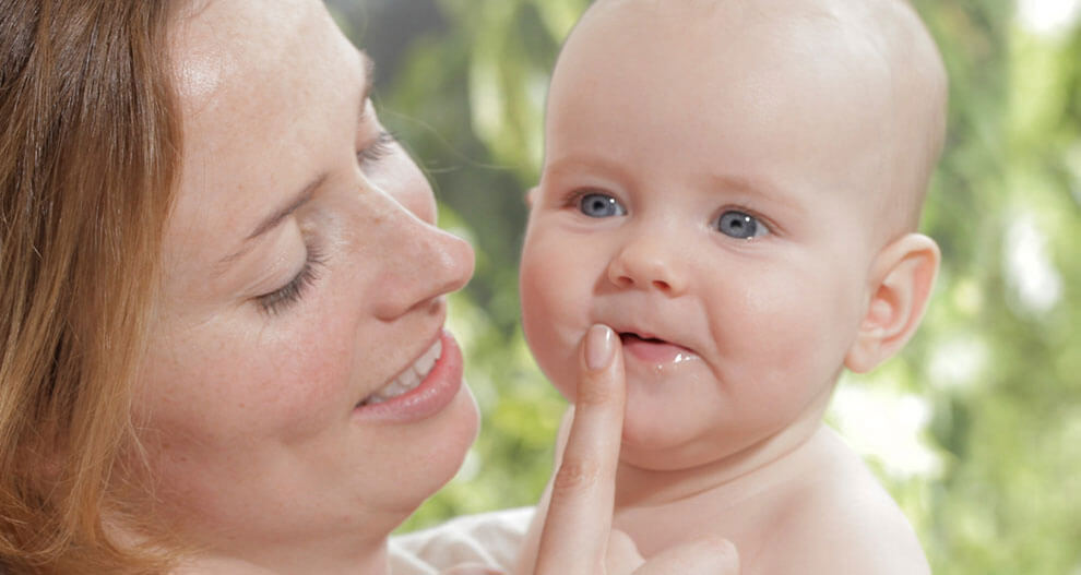 A woman is holding a baby, who is chewing on the woman's finger.
