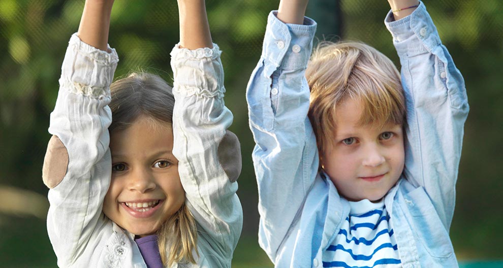 Two children, a girl and a boy, are raising their hands above their heads in a playful manner.
