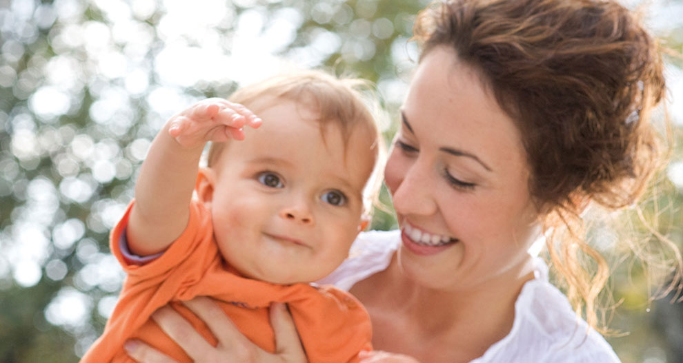 A woman lovingly holds a baby, both looking towards the camera.