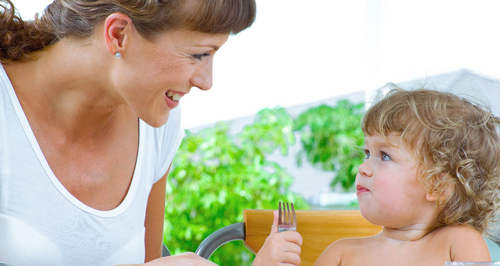 A woman and a child sit at a table, looking at each other.