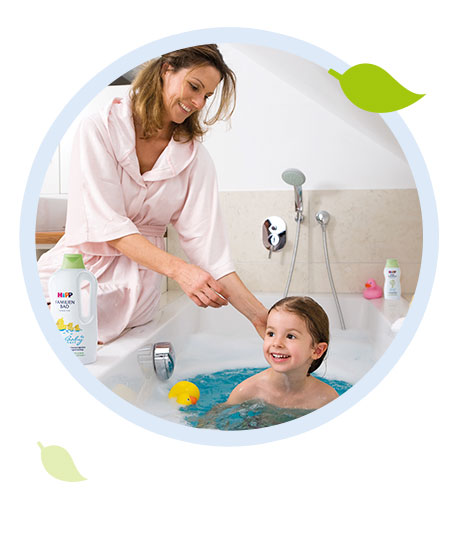 A woman in a pink robe is washing a child's hair in a bathtub.