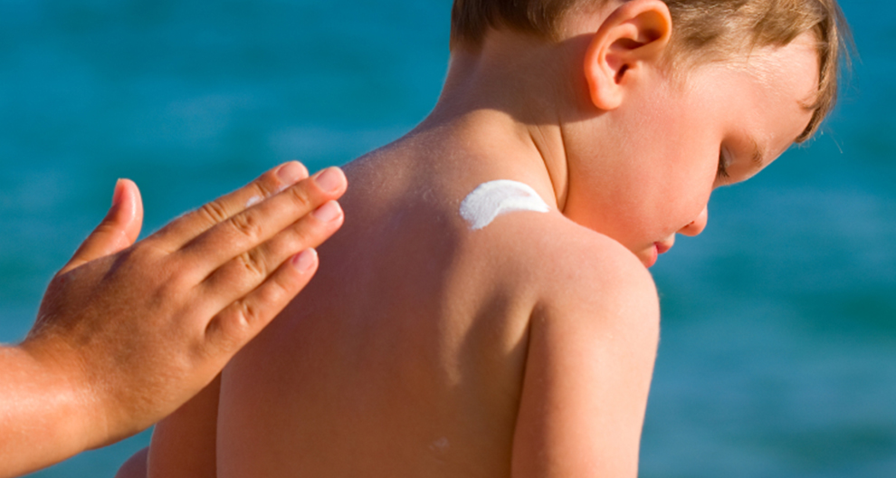 A child's back is being treated with sunscreen.