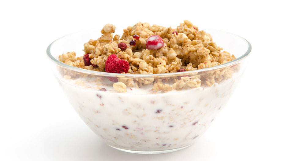 A bowl of granola with red berries and milk.
